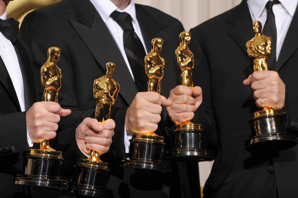 Five hands of men in tuxedos holding Oscars Trophies