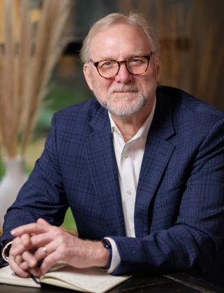 Bill Zipp sitting and smiling with hands clasped looking at viewer